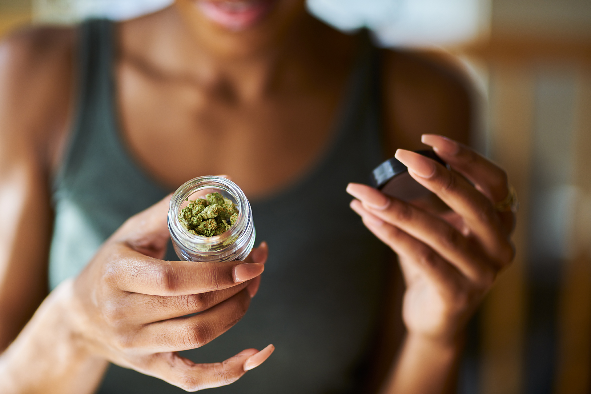 african american woman opening bottle of legal marijuana from dispensary close up with selective focus on weed