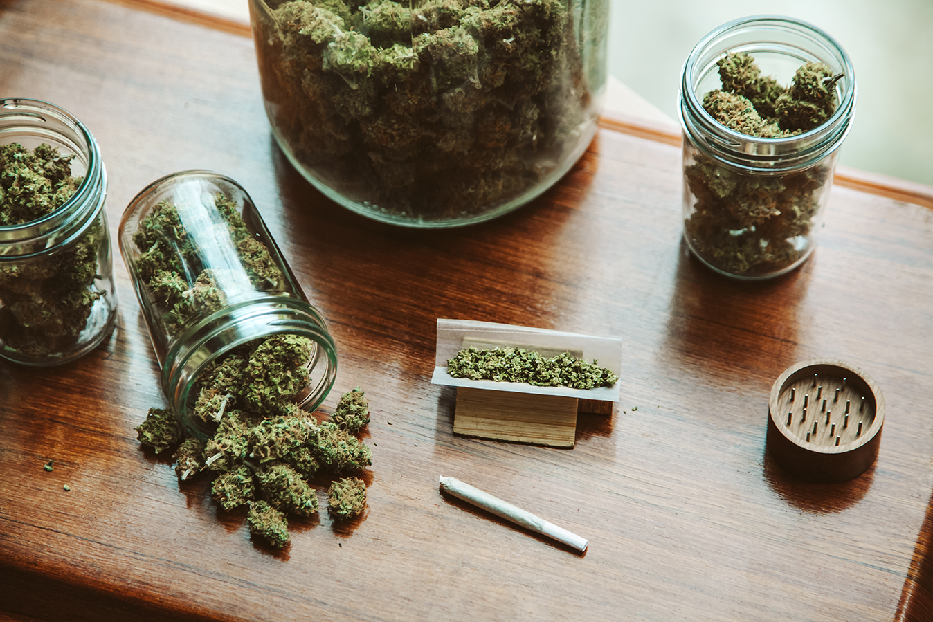 High angle view of glass jars full of marijuana plants with cannabis joint on wooden table